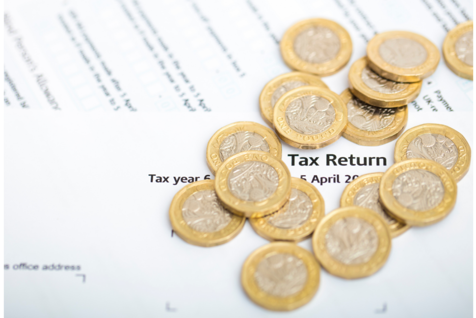 Pile of pound coins scattered over a tax return form with 'Tax Return' visible on the page.